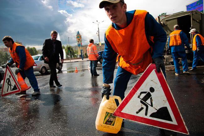 Рабочие в Долгопрудном наносят битумную мастику на дорожное полотно и устанавливают знаки дорожного движения.